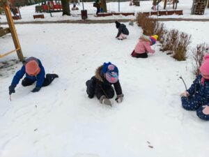 Czwórka dzieci maluje patykiem po śniegu
