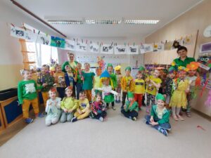 Grupa dzieci w żółtych i zielonych ubraniach w sali przedszkolnej.