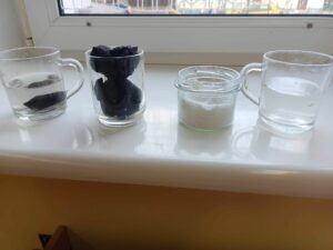 Szklanki na parapecie z zawartością (od lewej): węgiel w wodzie, węgiel, sól, woda z solą