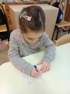 Dziewczynka w szarej bluzce podpisuje pocztówkę