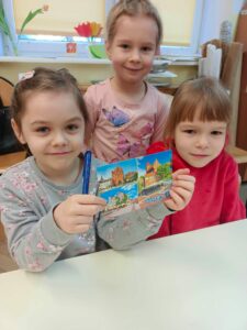Trzy dziewczynki, jedna z nich trzyma pocztówkę z Olsztyna