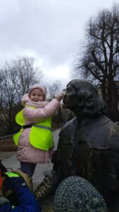 Dziewczynka w różowej kurtce trzymająca pomnik Mikołaja Kopernika za nos