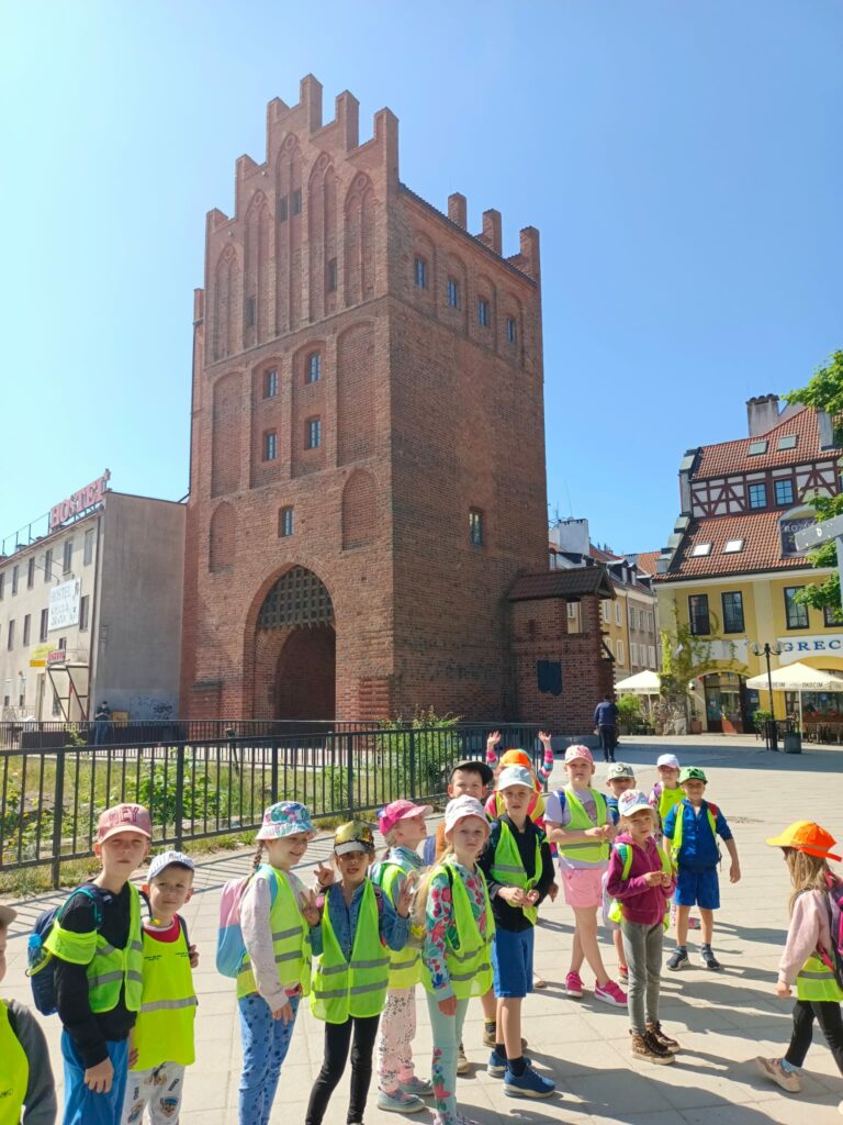 Grupa dzieci na tle Wysokiej Bramy w Olsztynie.