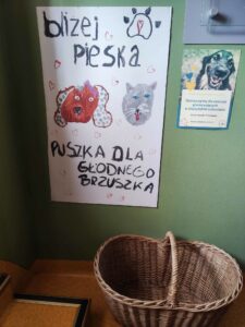 plakat nt. zbiórki i kosz wiklinowy w korytarzu przedszkola