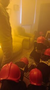 Dzieci w hełmach strażackich w zadymionym pomieszczeniu.