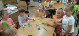 Dzieci siedzą przy stoliku, trzymają marchewki wyciete z papieru.