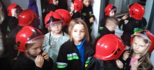 Grupa dzieci w hełmach i kurtkach strażackich.