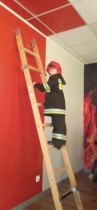 Chłopiec w stroju strażaka wchodzi po drabinie