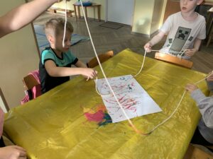 grupa dzieci malująca farbami na pomocą sznurka