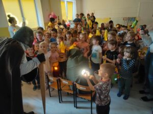 Dzieci z latarenkami witające św. Marcina. Na krześle przed dziećmi żebrak