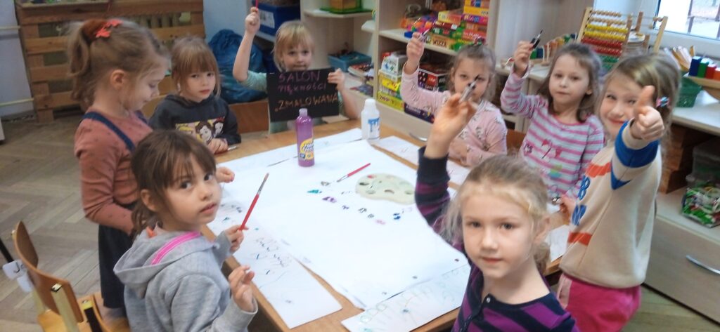 Grupa dziewczynek siedząca przy stoliku maluje farbami.