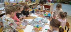 Grupa dzieci pracuje przy stoliku; wycina, rysuje, konstruuje z klocków.