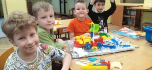 Grupa chłopców siedzi przy stoliku, na którym znajduje się konstrukcja z klocków LEGO