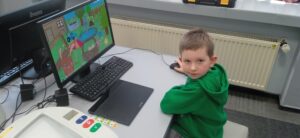 Chłopiec w zielonej bluzie siedzi przed monitorem.