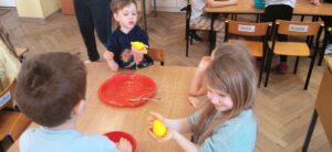 Grupa dzieci siedzi przy stoliku i formuje jaja z żółtej masy.