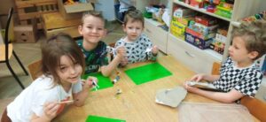 Czterech chłopców siedzi przy stoliku i maluje figurki dinozaurów.