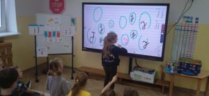 Dziewczynka pisze na tablicy interaktywnej literę "J".