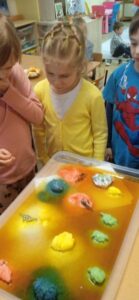 Dziewczynka w żółtym sweterku obserwuje proces rozpuszczania się sodowych, kolorowych jaj.