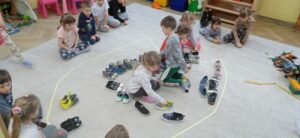 Dzieci ustawiają buty na dywanie, na którym widoczny jest kontur łapy dinozaura.