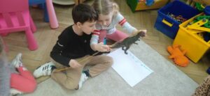 Dwoje dzieci mierzy figurkę dinozaura.