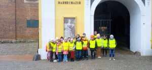 Grupa dzieci w odblaskowych kamizelkach stoi przed budynkiem muzeum.