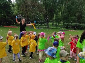 nauczycielka puszczająca bańki grupie dzieci w kolorowych koszulkach