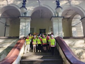 Grupa dzieci w odblaskowych kamizelkach stoi na schodach przed wejściem do budynku.