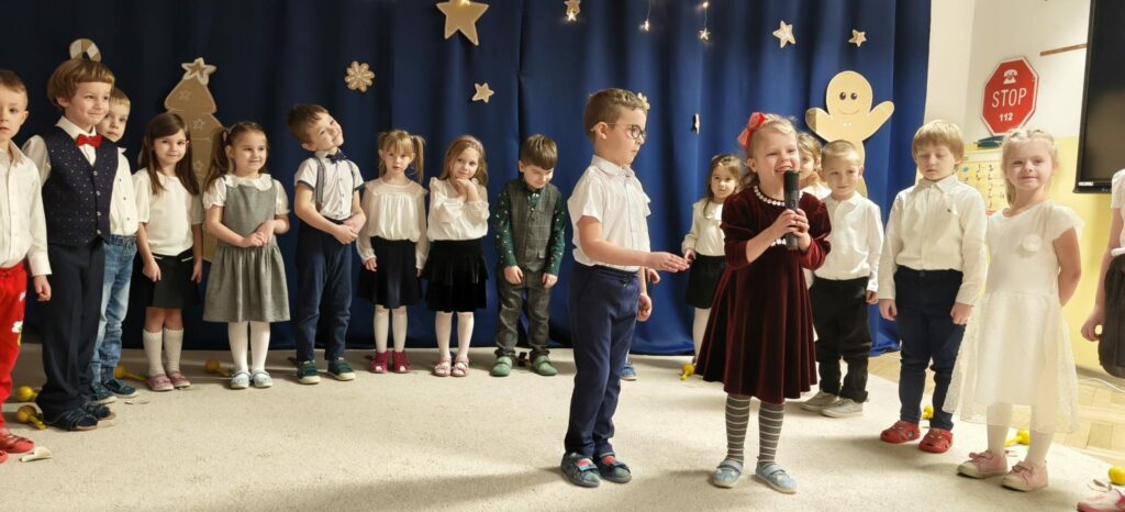 Grupa dzieci w strojach galowych podczas występu artystycznego.