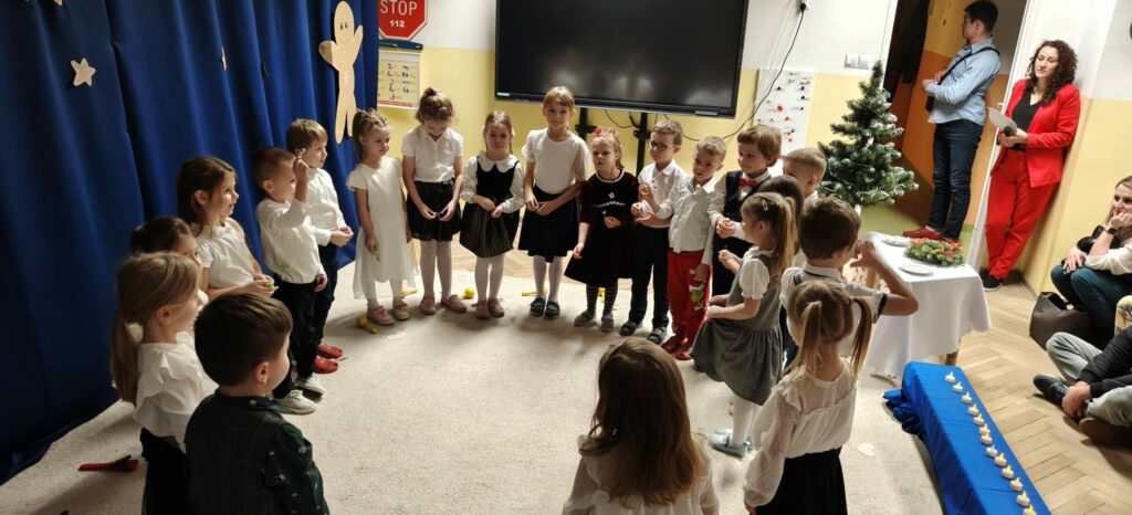 Grupa dzieci w strojach galowych podczas występu artystycznego.