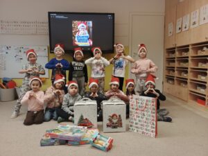 Dzieci w czapach mikołajowych prezentują paczki świąteczne.