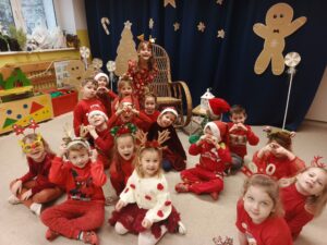 Grupa dzieci w sali przedszkolnej, w tle świąteczne dekoracje.