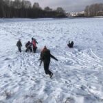 grupa dzieci biega po śniegu, jedno dziecko zjeżdża na sankach