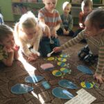 dzieci na dywanie mieszają "marcową zupę", na dywanie porozkładane symbole pogodowe i garnek