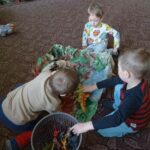 Troje dzieci bawi sie na dywanie dinozaurami
