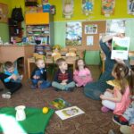 dzieci i nauczycielka siedzą w kole, nauczycielka pokazuje ilustrację ślimaka