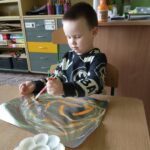 chłopiec maluje farbami po foli aluminiowej