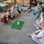 Dzieci siedzą na dywanie i słuchają nauczycielki.