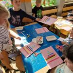 Dzieci przyklejają kolorowe paski na kartkę.