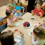 Dzieci siedzą przy stolikach i jedzą owoce