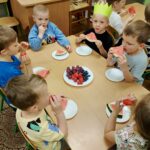 Dzieci siedzą przy stolikach i jedzą owoce