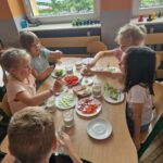 Dzieci robią sobie same kanapki z warzywami, jajkiem, szynką i ciemnym chlebem.