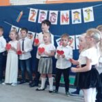 grupa dzieci w strojach galowych stoi przed dekoracją