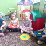 grupa dzieci siedzi na dywanie, przed nimi krążki