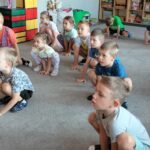 Dzieci kucają na dywanie jak żabki