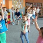 Dzieci stoją na dywanie i wykonują krążenia ramion w przód