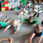 Dzieci leżą na dywanie na brzuchu z uniesionymi rękoma i nogami