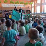 grupa dzieci siedzi na dywanie, przed nimi dwie aktorki