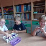 troje dzieci siedzi przy stoliku, robią kulki z bibuły