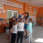 grupa dzieci trzyma w ręku piłkę i dotyka piłki instruktora