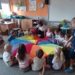 grupa dzieci siedzi na dywanie, bawi sie chustą